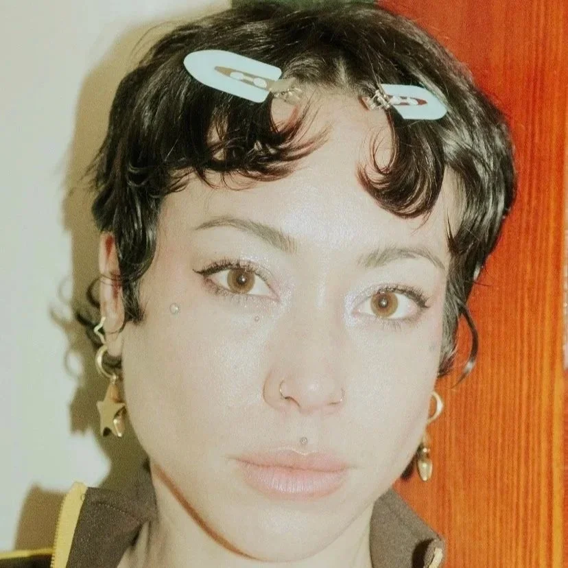Close-up portrait of artist Caro Garofalo wearing hair clips and multiple earrings.