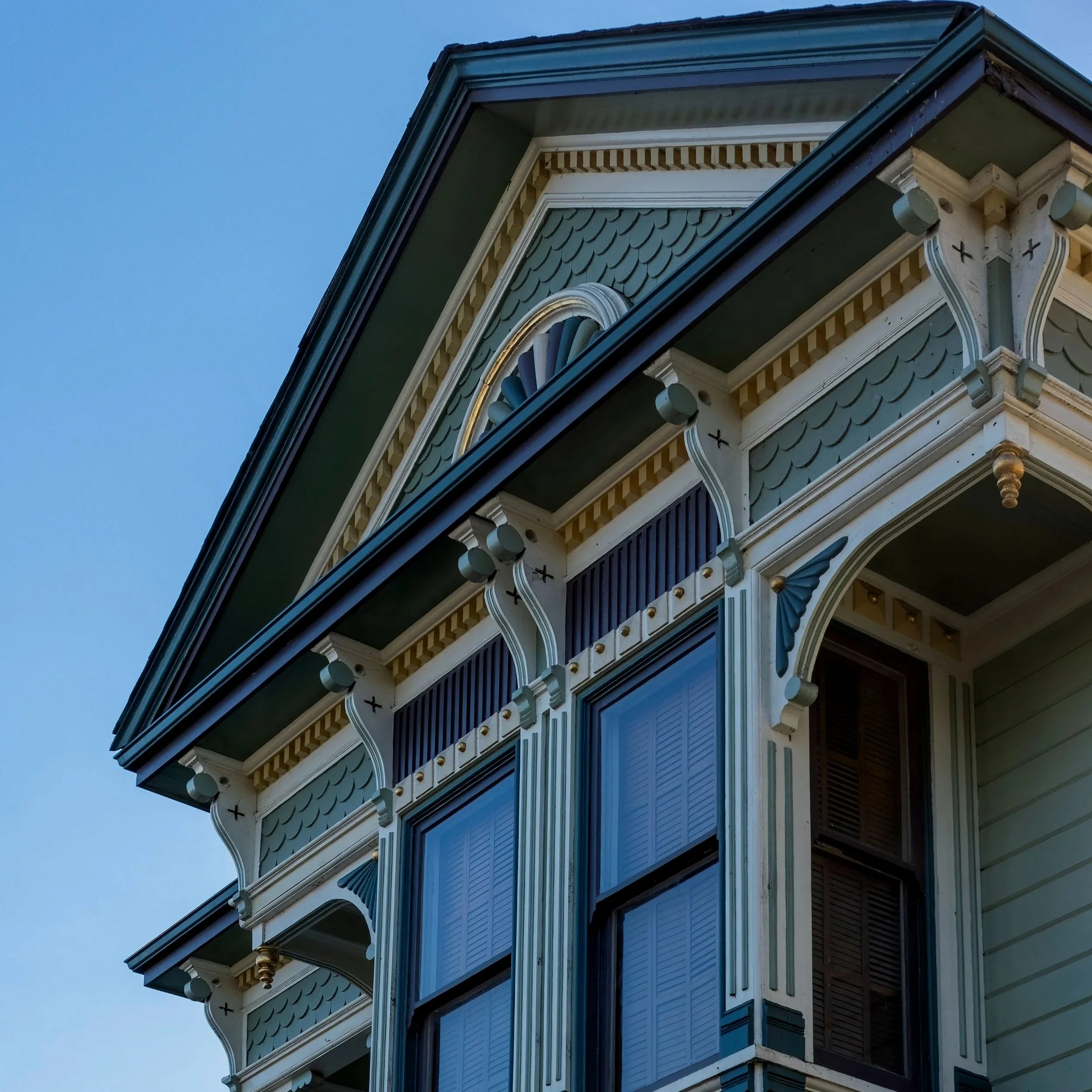 Roofline peak of Queen Anne house, painted in shades of blue with white and gold accents