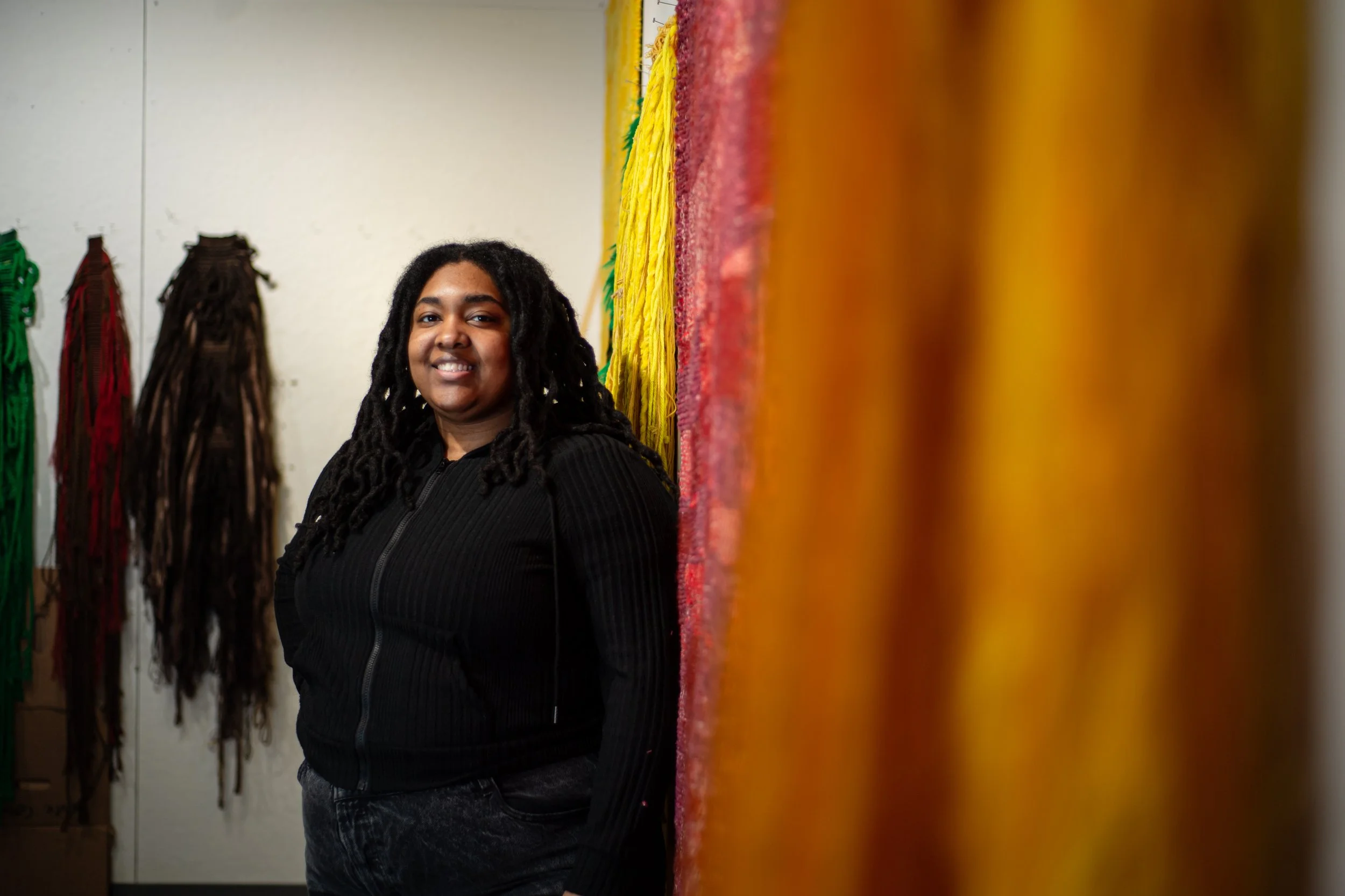 Artist Cashay Johnson standing in a studio surrounded by colorful fiber artworks.