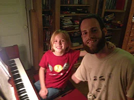 Young piano student Millie and her teacher Andrew smiling at the piano during a Brooklyn lesson.