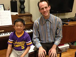 Young piano student Theo and his teacher Andrew sitting together at the piano at Theo's home.