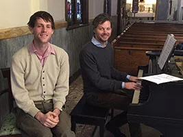 Adult student Nicholas and teacher Andrew sitting beside a piano at a Brooklyn church performance space.