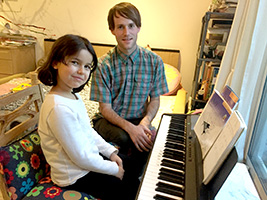 Piano teacher Andrew with young student Linda sitting at the keyboard during a light-hearted lesson.