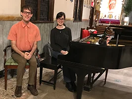 Adult piano student Rachel and her teacher Andrew seated by a grand piano after a Brooklyn lesson.