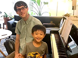 Young piano student Luca smiling with his teacher Andrew during a fun lesson in Brooklyn.