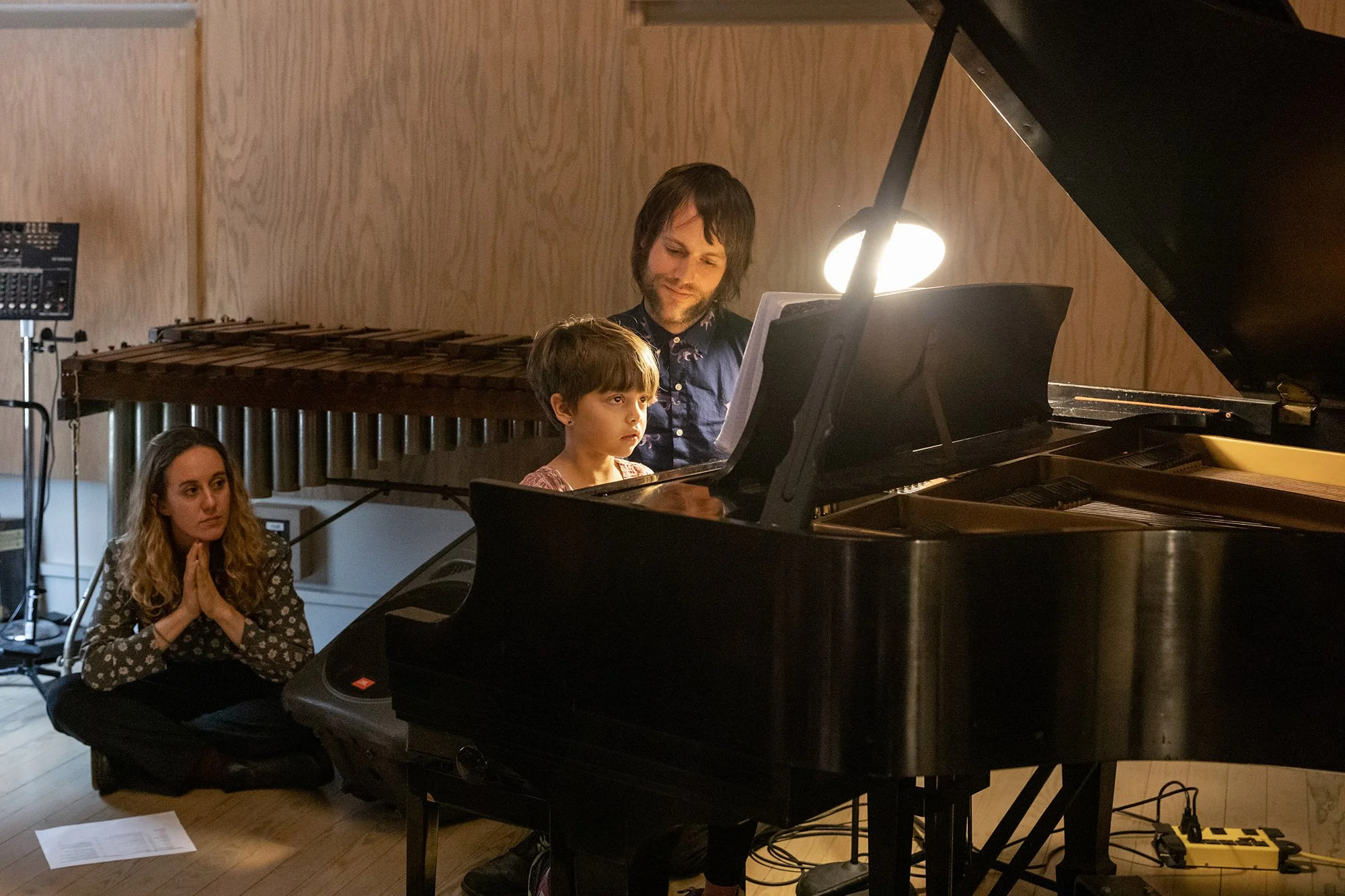 Piano teacher guiding a young student at a grand piano during a recital.