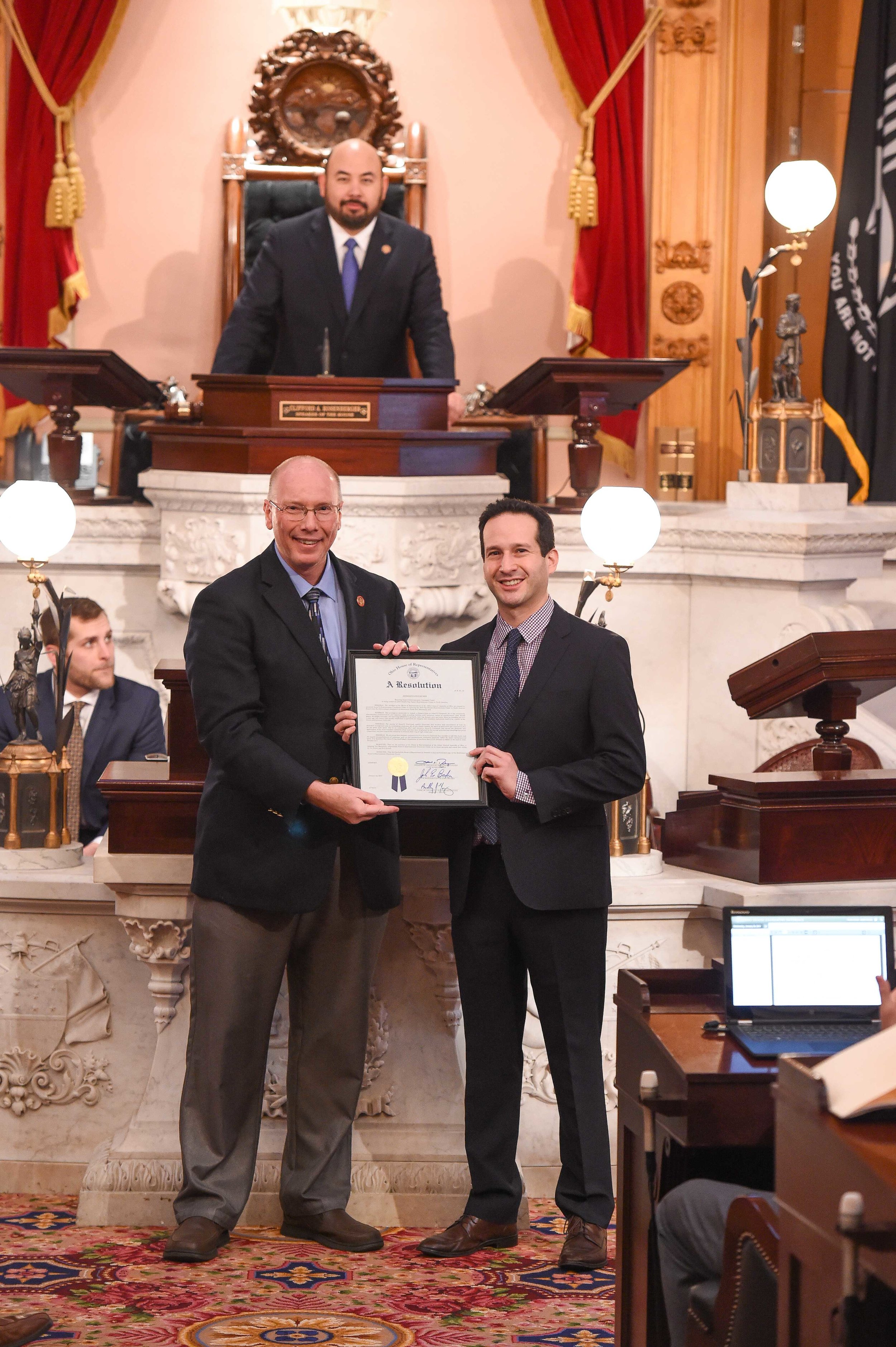 Ohio State Representative John Becker (R-Union Township) presents the resolution to Scene75 Entertainment CEO Jonah Sandler with Speaker of the Ohio House of Representatives Cliff Rosenberger presiding in the chambers.