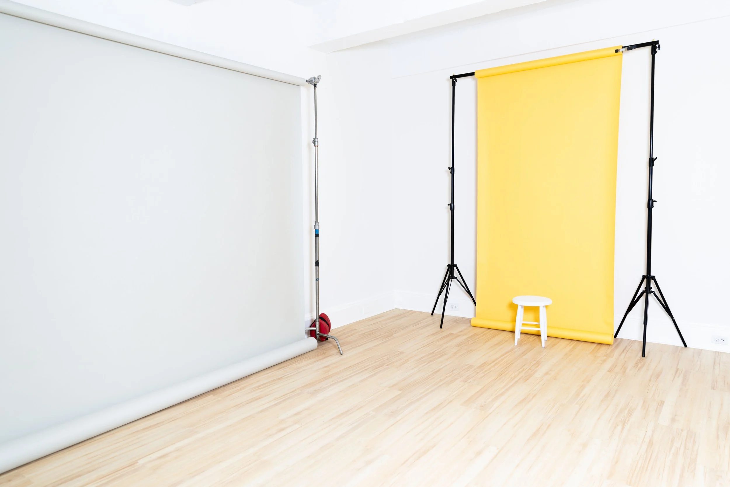 Photography studio with white background, yellow backdrop, small white stool, and light wood flooring.