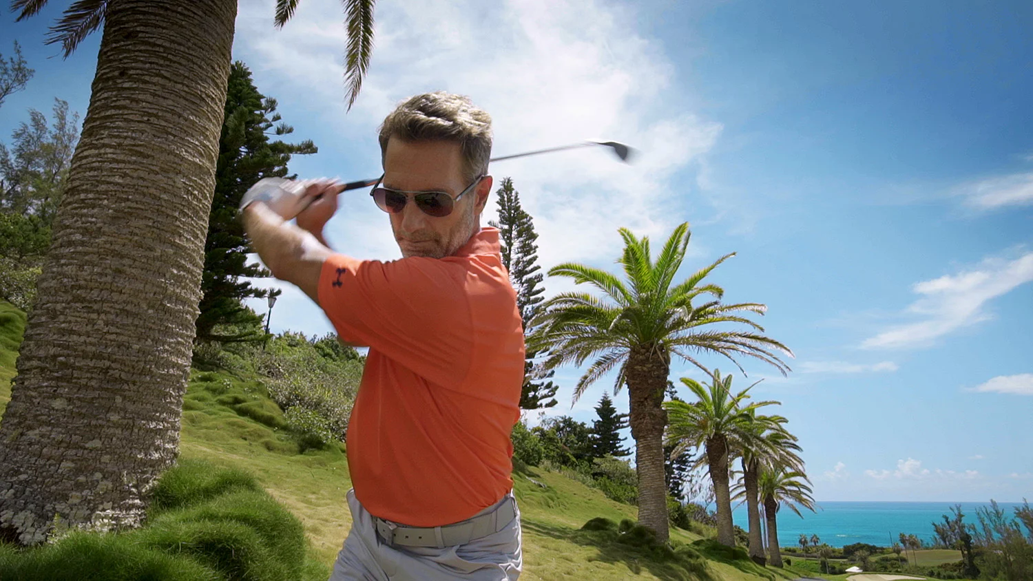 Man swinging golf club near the ocean.