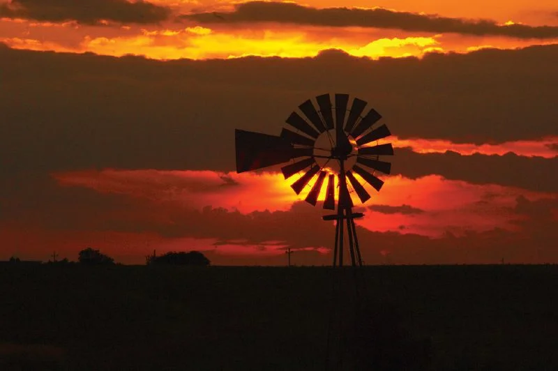 The sun sets behind a windmill in Union County south of Winterset, Iowa.