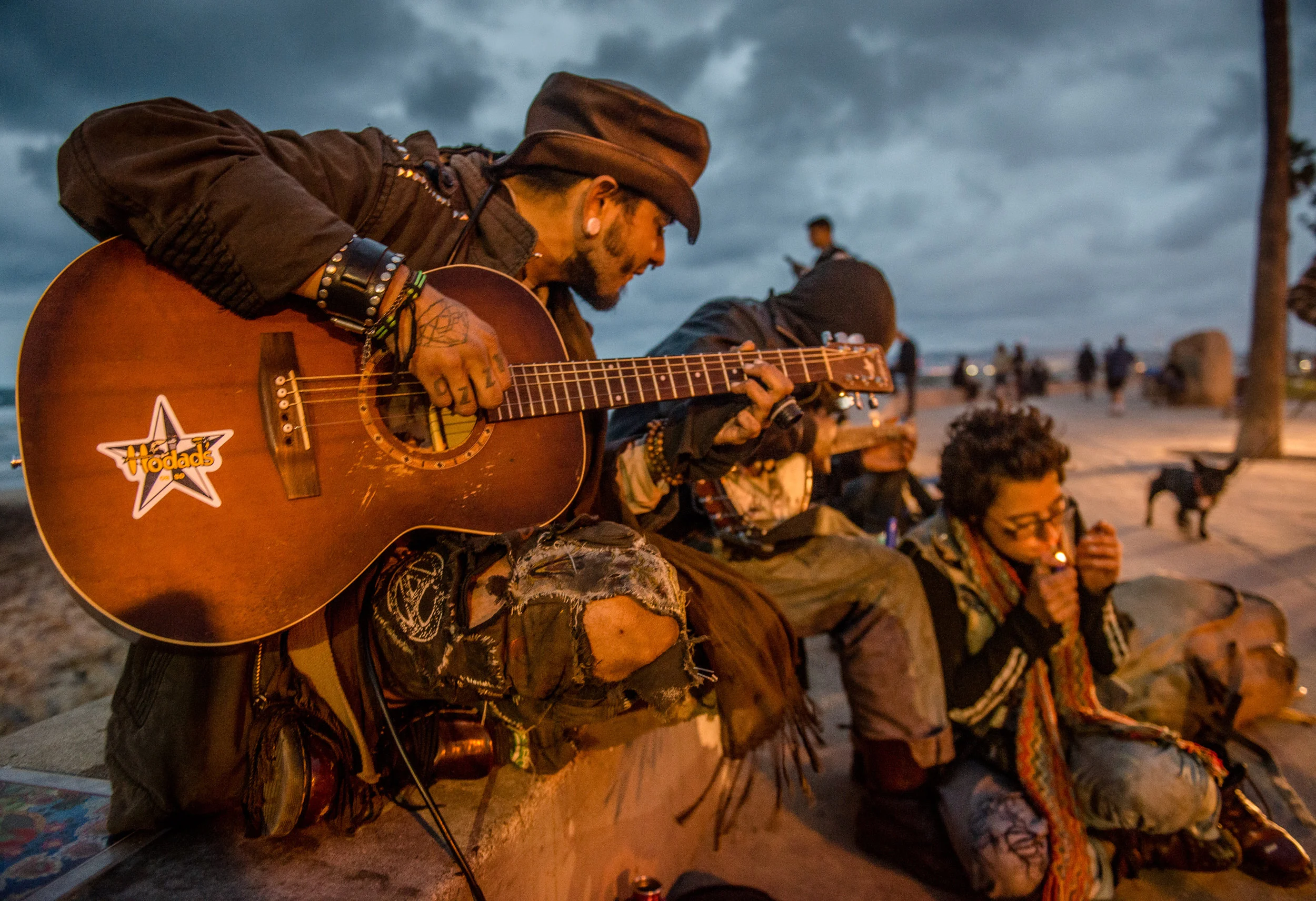 Ozzy a self-described volunteer homeless man plays guitar as friends listen near the water at Ocean Beach, California. Ozzy has traveled across the country via auto, train and foot. Last night he was happy to be reunited with old friends that he had accidentally crossed paths with again.