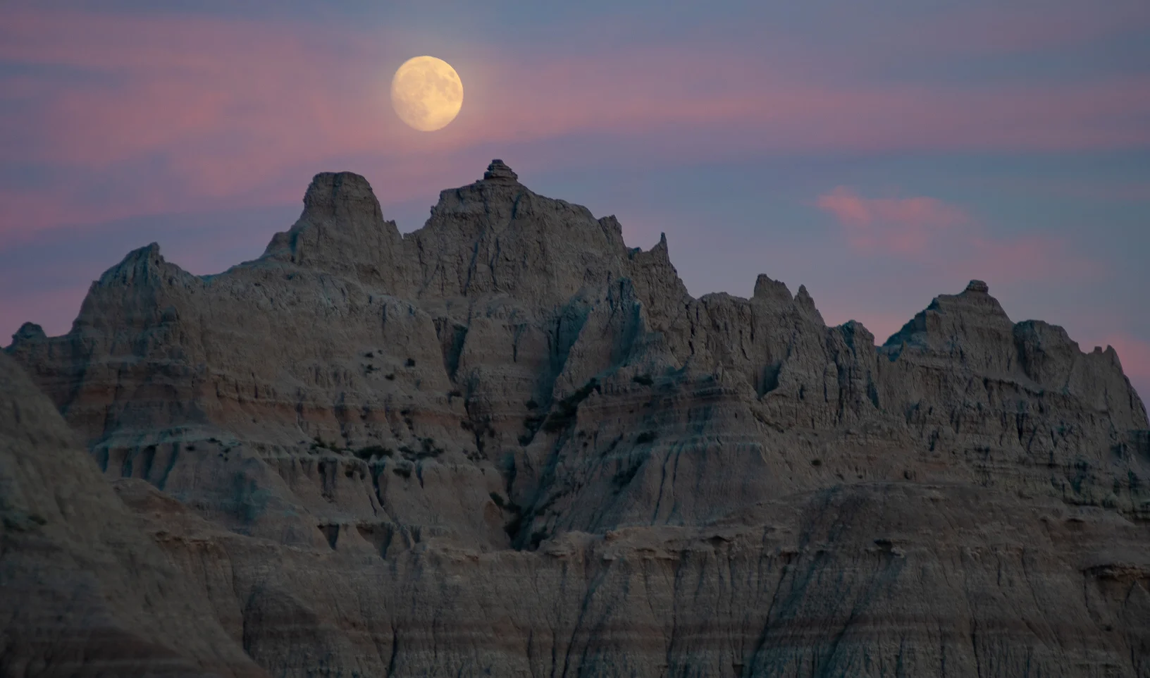 The moon shines bright over rock formations at Badlands National Park in South Dakota.