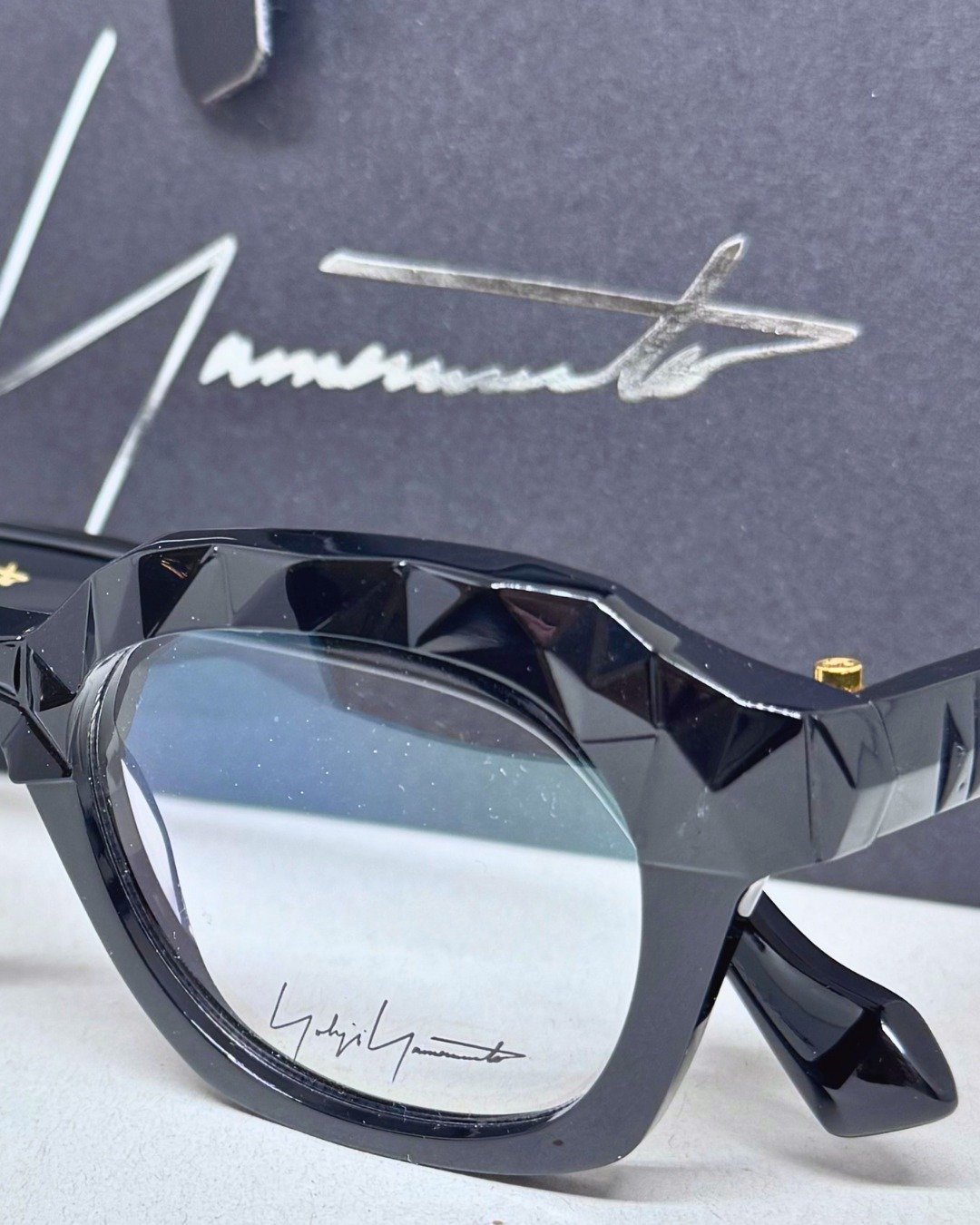 Most people look at the lens. This frame wants you to look closer.

Swipe to see the part most people walk past.

The temples on this Yohji Yamamoto frame are faceted &mdash; cut with geometric precision, like the surface of crystal. Gold hardware. T