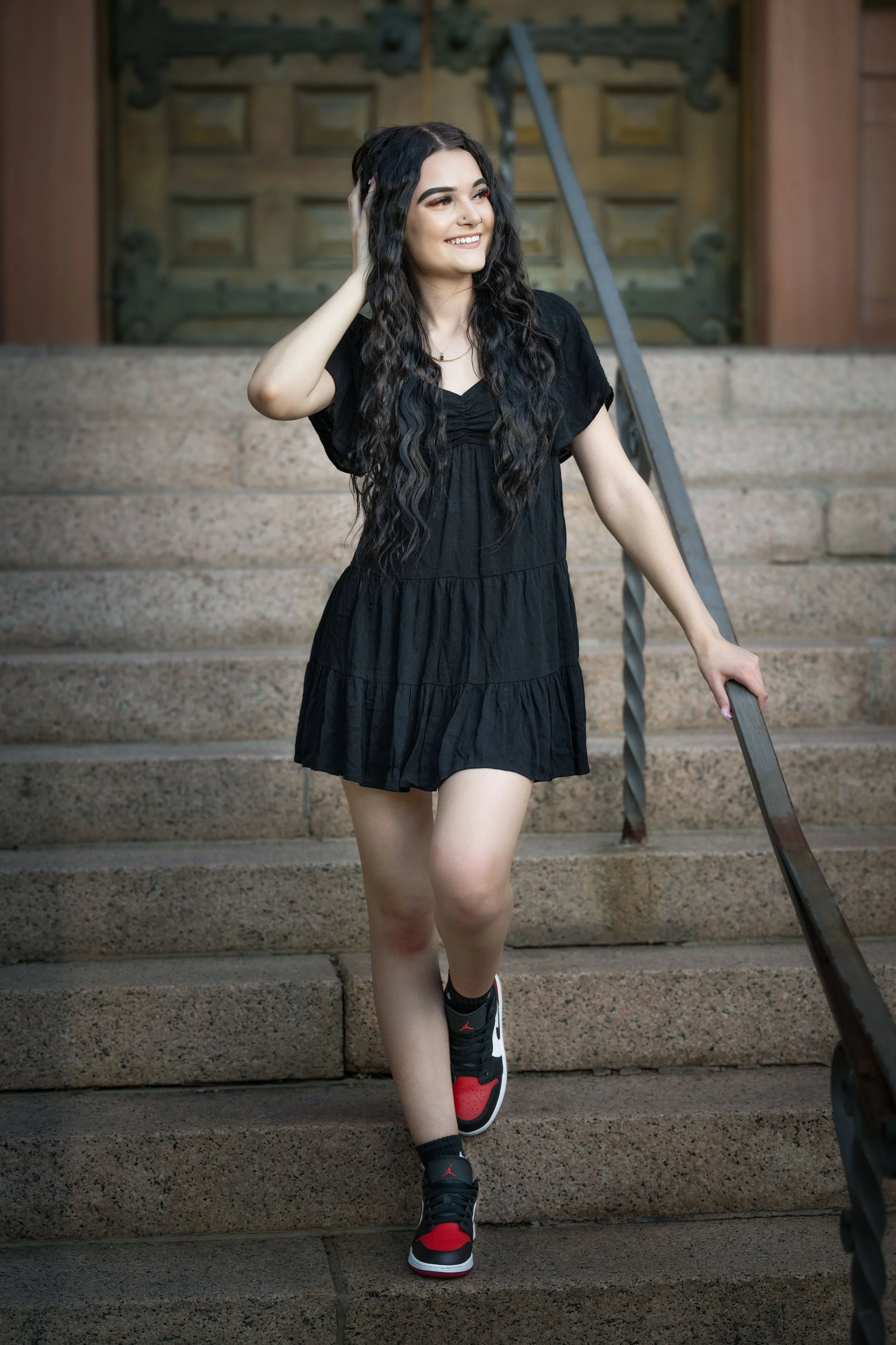 Young woman with long curly hair walking down stairs, smiling, wearing a black dress and sneakers