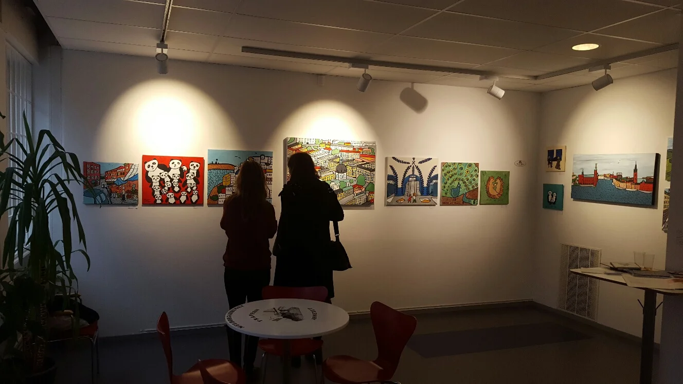 Några besökare står och beundrar min medutställare och konstnärsväns, Orsi Milds tavlor.