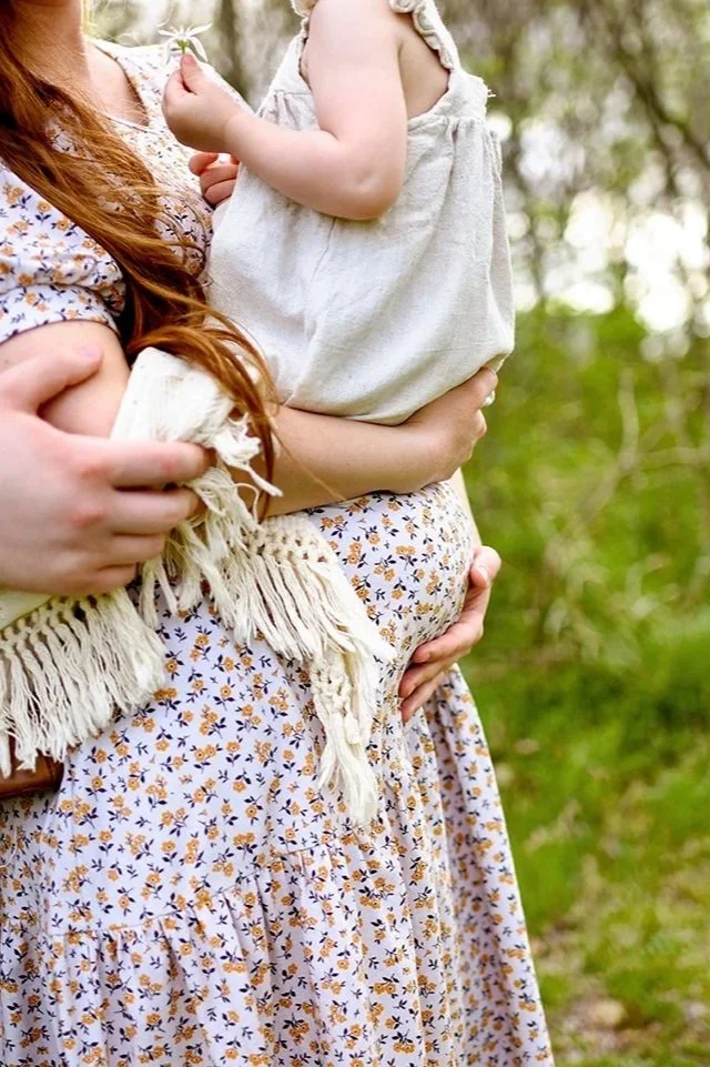 close up of belly bump with older sibling and mom and dads hands