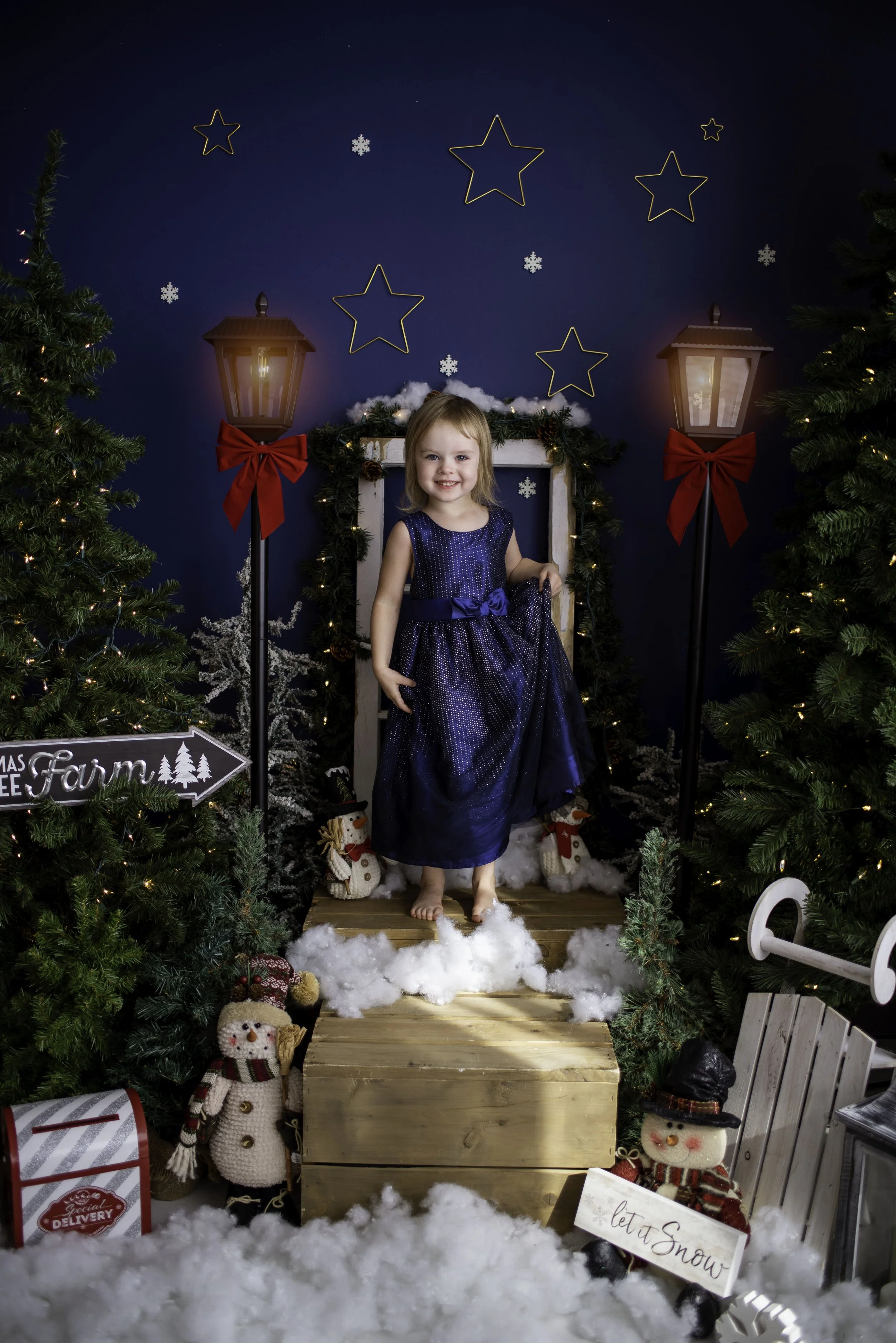 little girl stands on steps surrounded by trees snow and snowmen