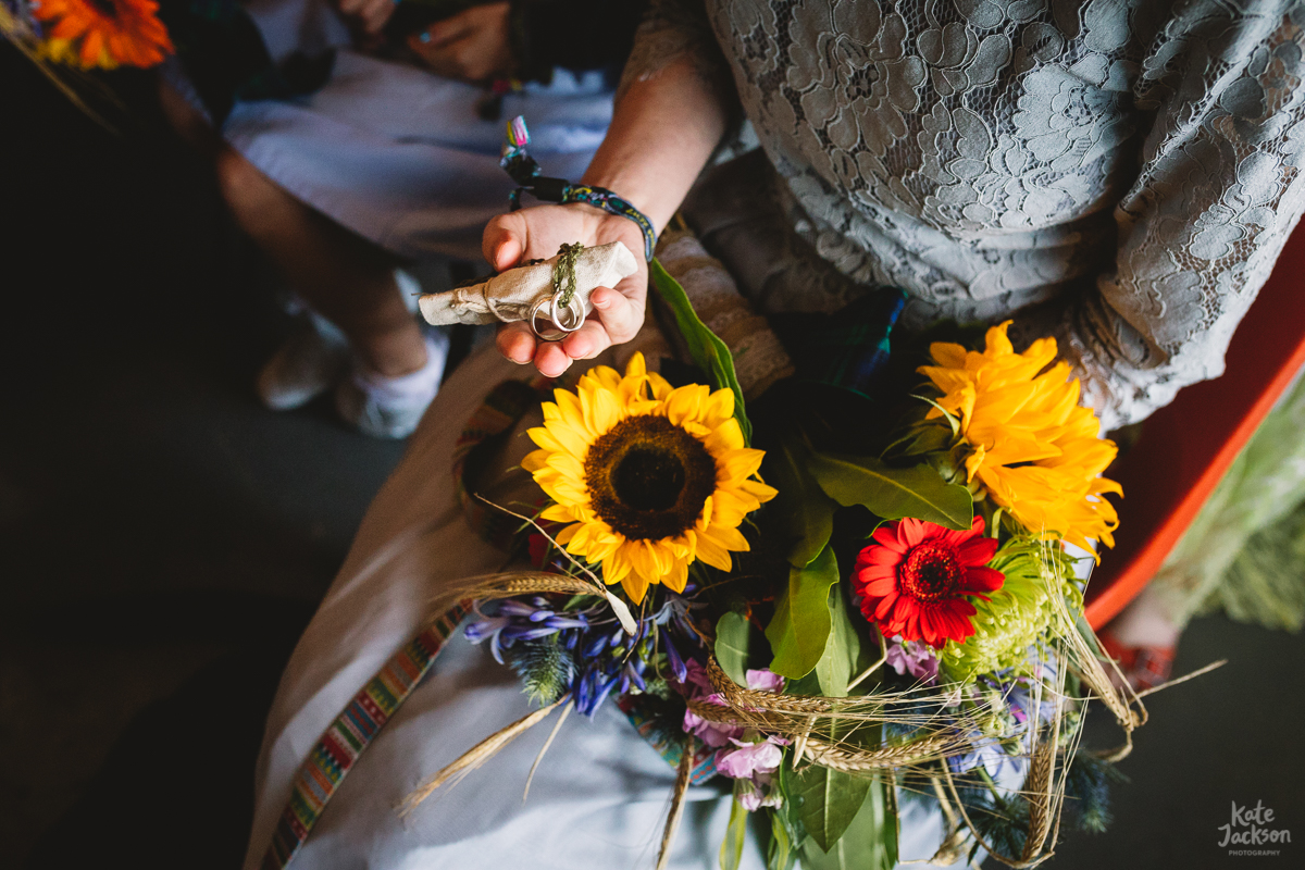 Wedding ring blessing at humanist festival wedding, photo of bridesmaids hand with the wedding rings and her diy bouquet of sunflowers and other summer flowers