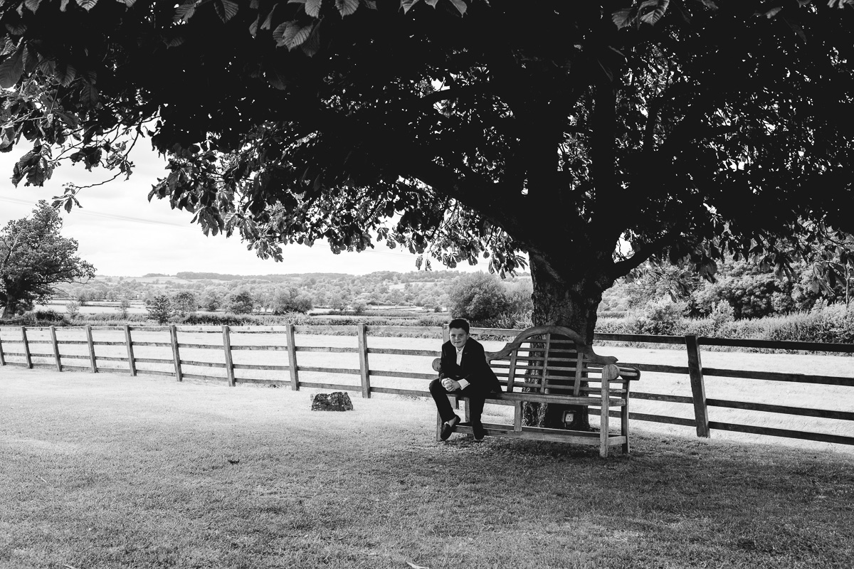 Man relaxes on bench at relaxed Hyde Barn Wedding