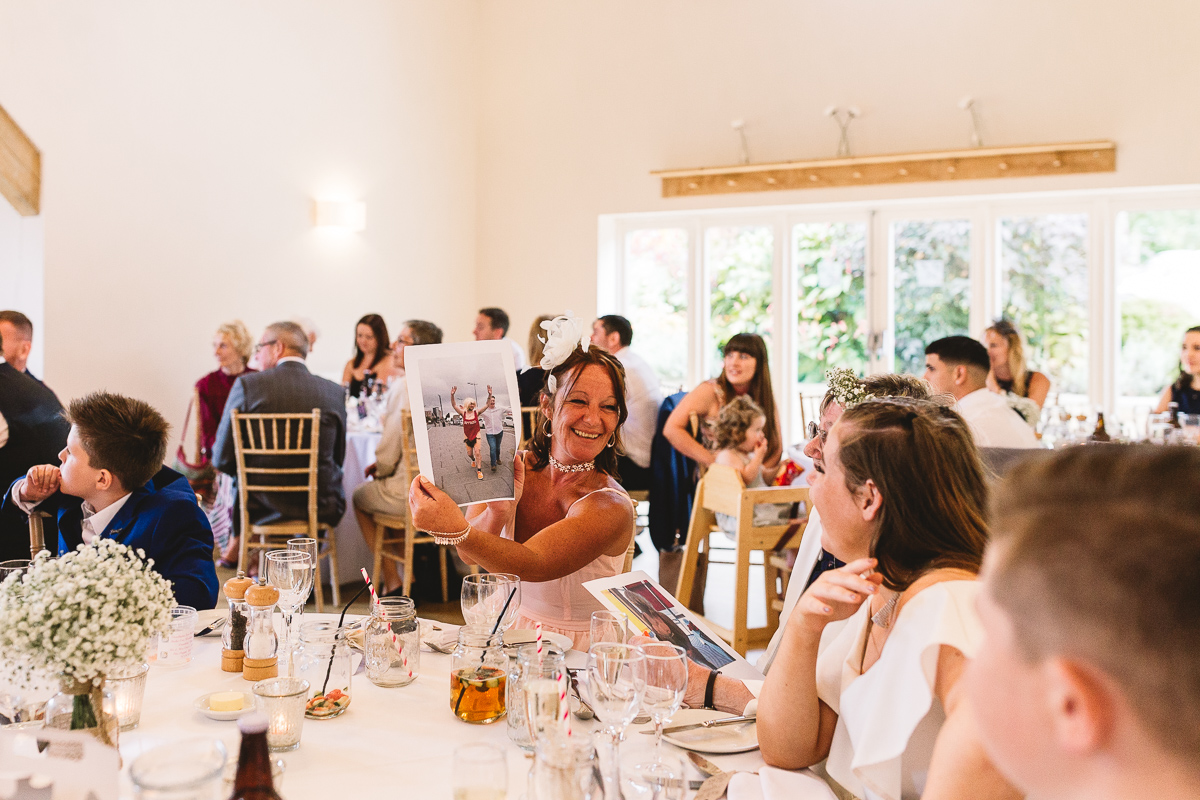 Lady holds out fun photo of groom on stag party during wedding speeches