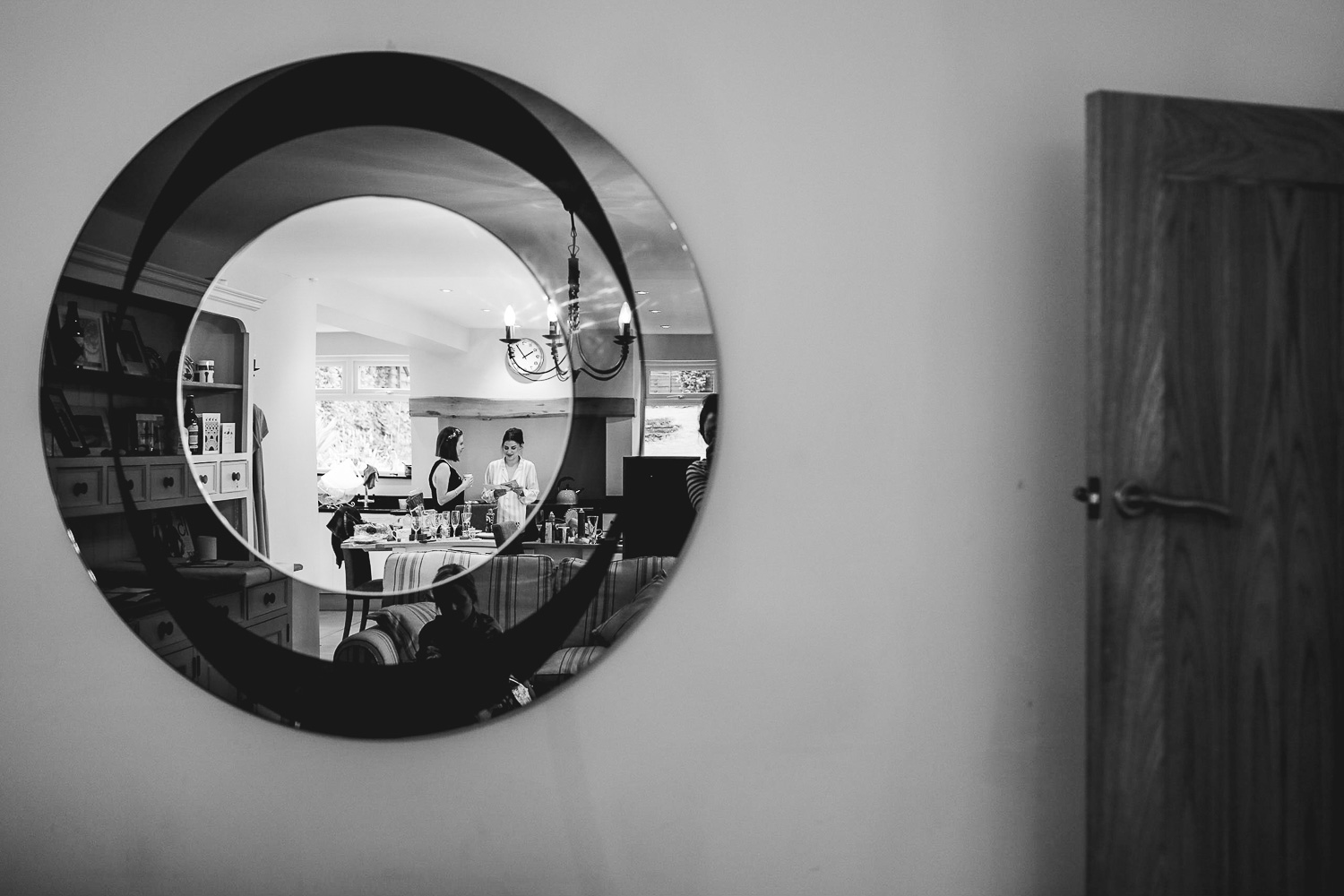 Documentary photograph of mirror where you can see the bride with a bridesmaid in pyjamas in the kitchen in the reflection at relaxed Sheffield wedding