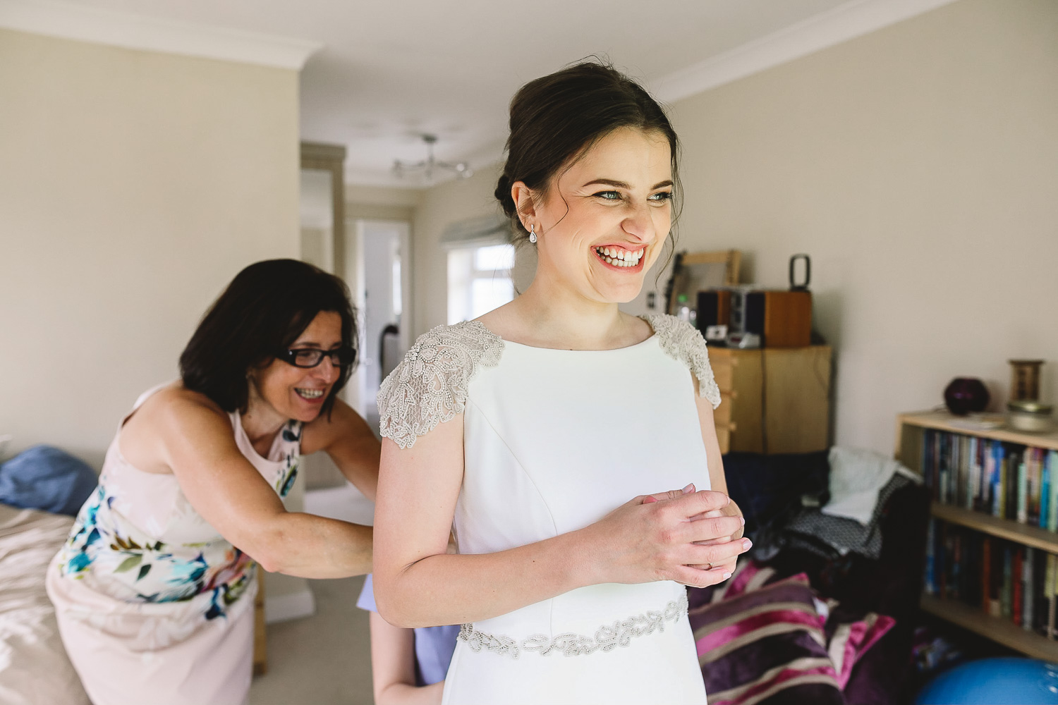 Photo of bride smiling and excited in her Rosa Clara wedding dress whilst her mum and sister are in the background doing the back up at relaxed Sheffield wedding.