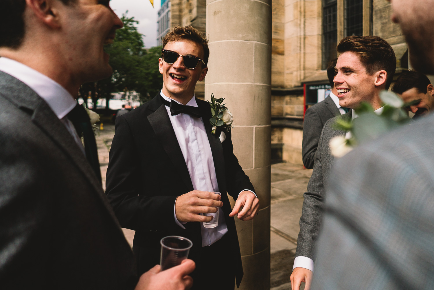 Groom in tux and sunglasses laughing and having fun with Groomsmen outside of Sheffield wedding venue before the ceremony in Sheffield