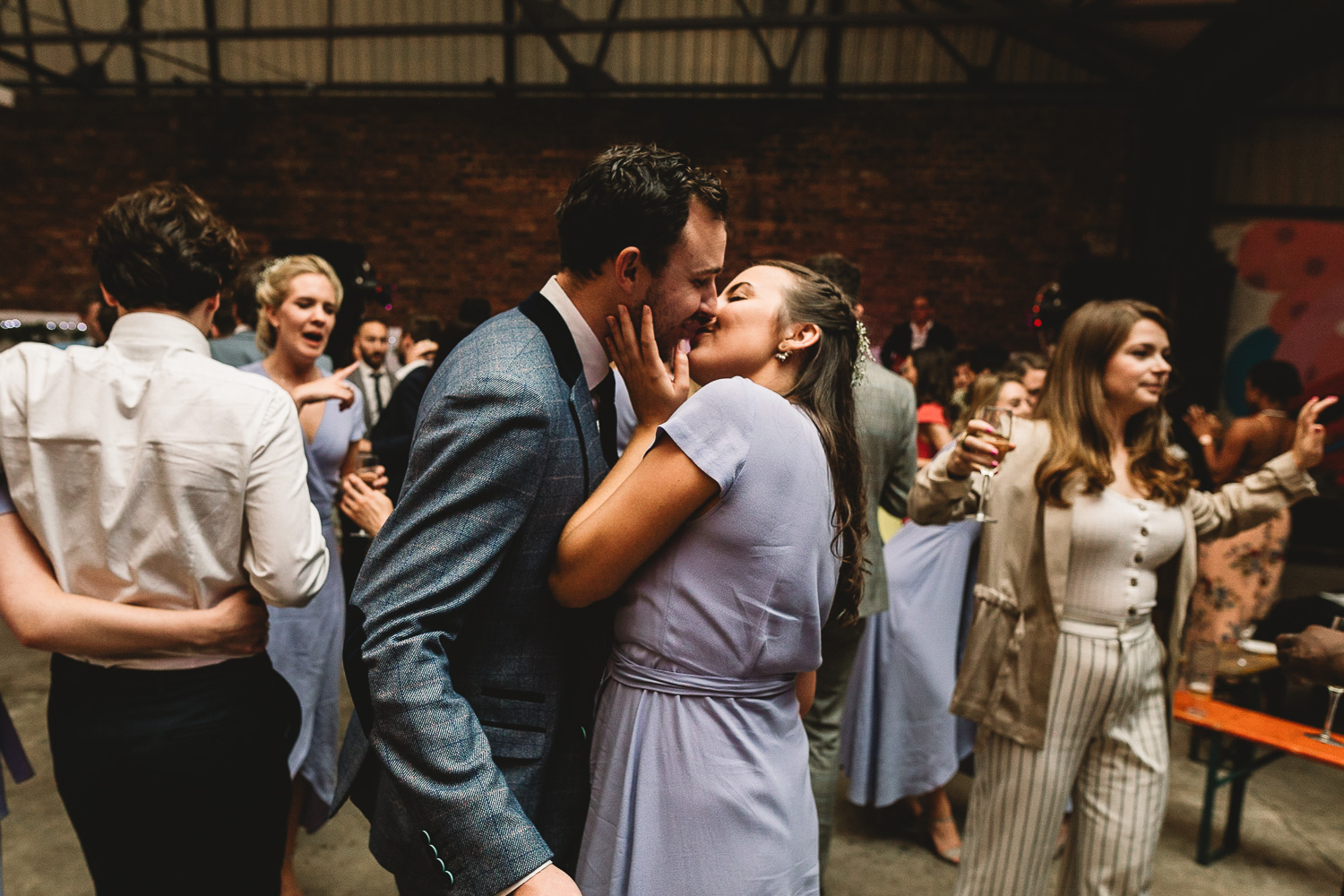 Bridesmaid in lilac dress kissing a man in a cool blue suit at alternative warehouse wedding venue 92 burton road