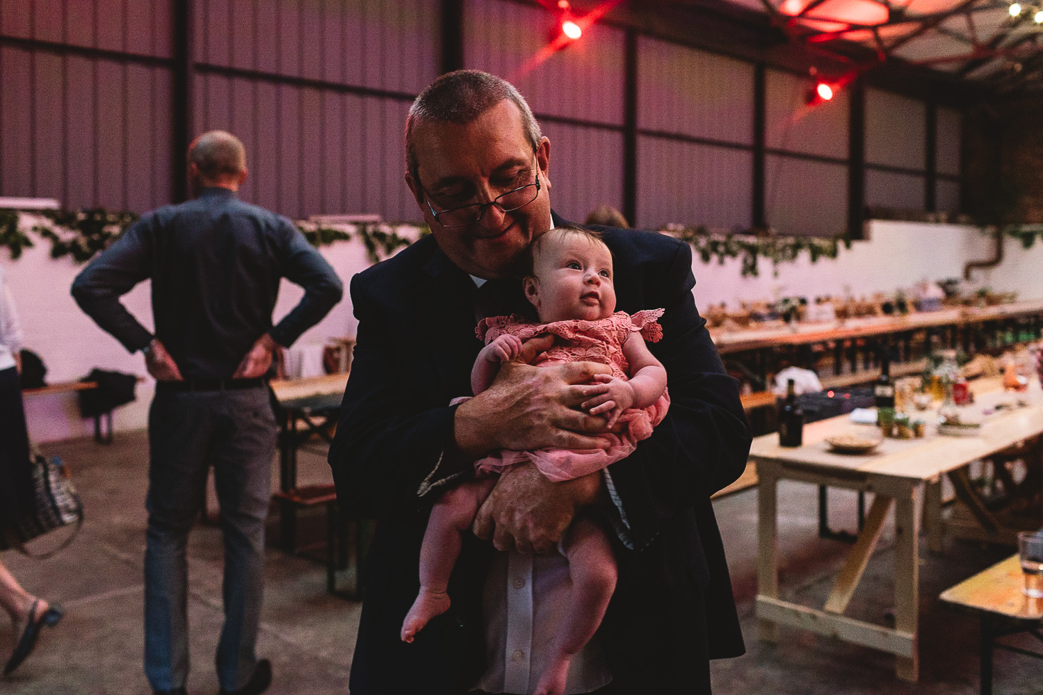 Man holding baby who is looking up at the colourful lighting in warehouse wedding venue 92 Burton Road in Sheffield