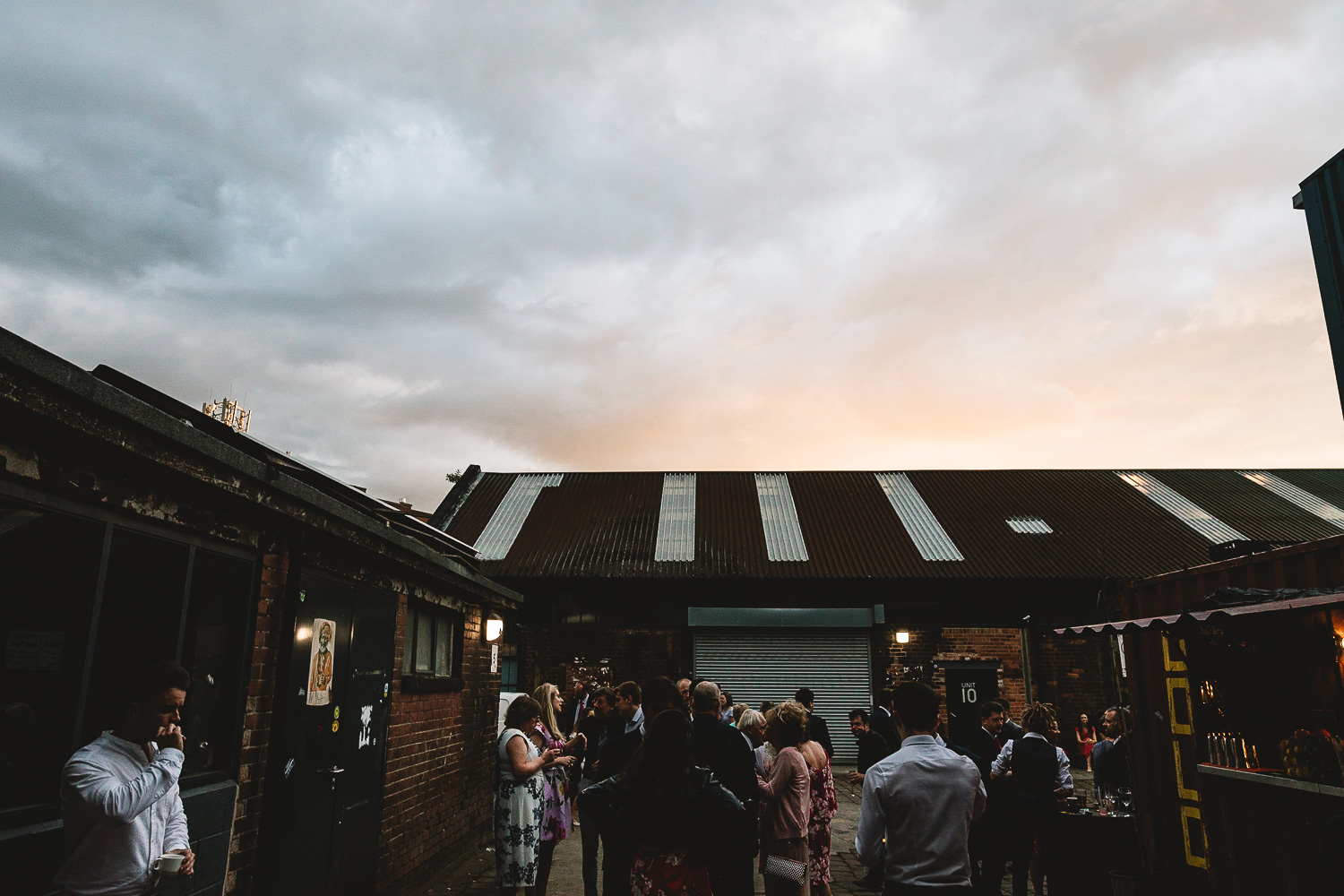 Photo of pink sunset over warehouse buildings at 92 burton road wedding venue with guests stood outside chatting