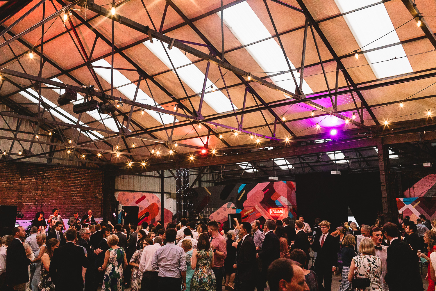 Wide photo of the dance floor flowing full of guests having fun dancing in warehouse wedding venue 92 Burton Road in Sheffield