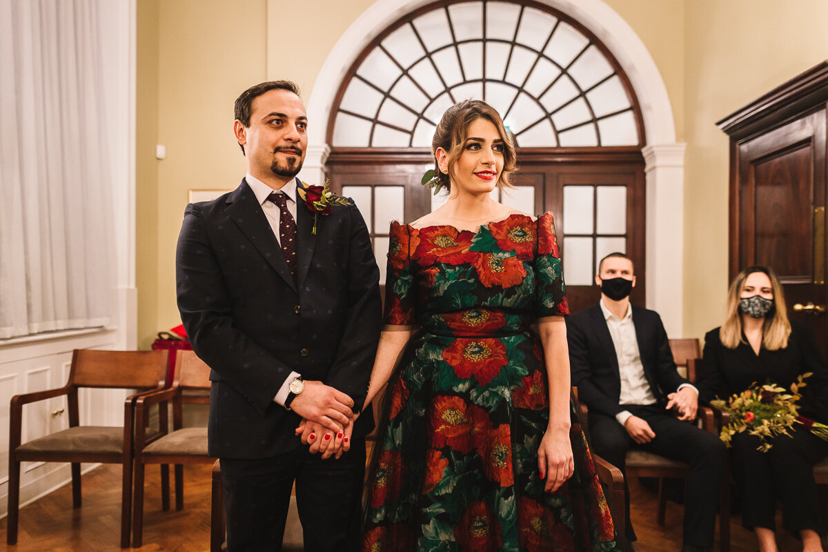 Bride and Groom holding hands with two guests in face masks in the background during super small micro wedding in 2020 at Chelsea Town Hall in London | Kate Jackson Photography-1.jpg