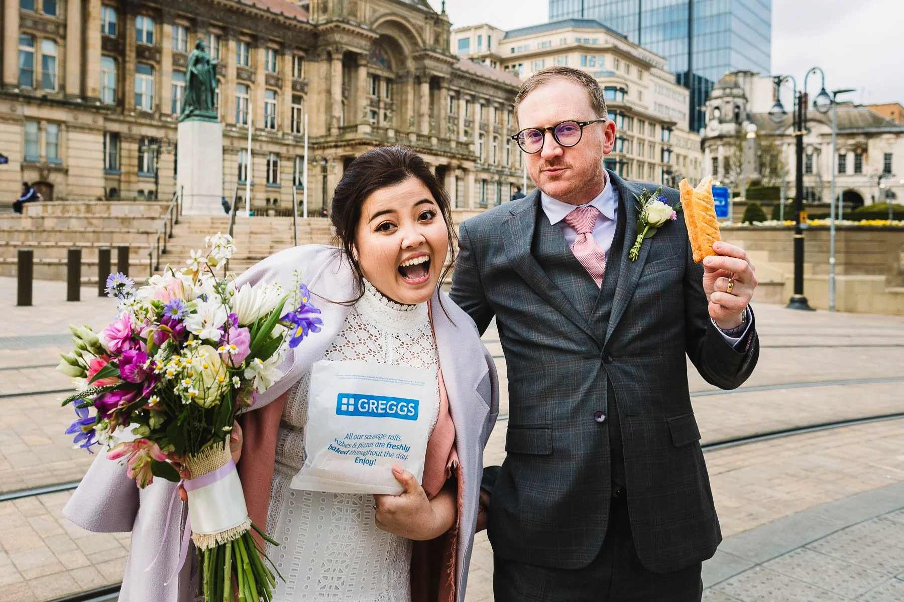 Newlyweds laughing with a Greggs sausage roll after their Birmingham city centre wedding