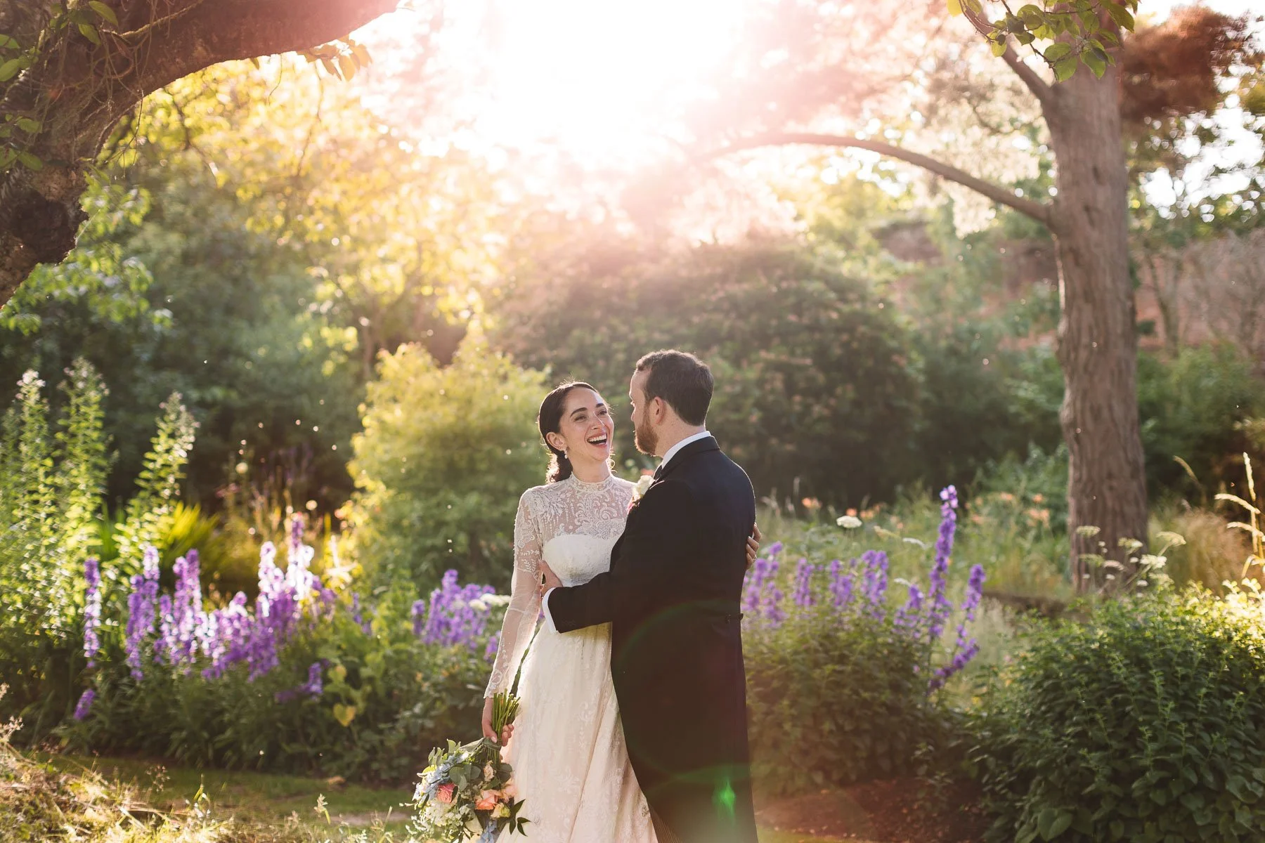 Bride and groom laughing together in the sunlit gardens at Walcot Hall on their wedding day