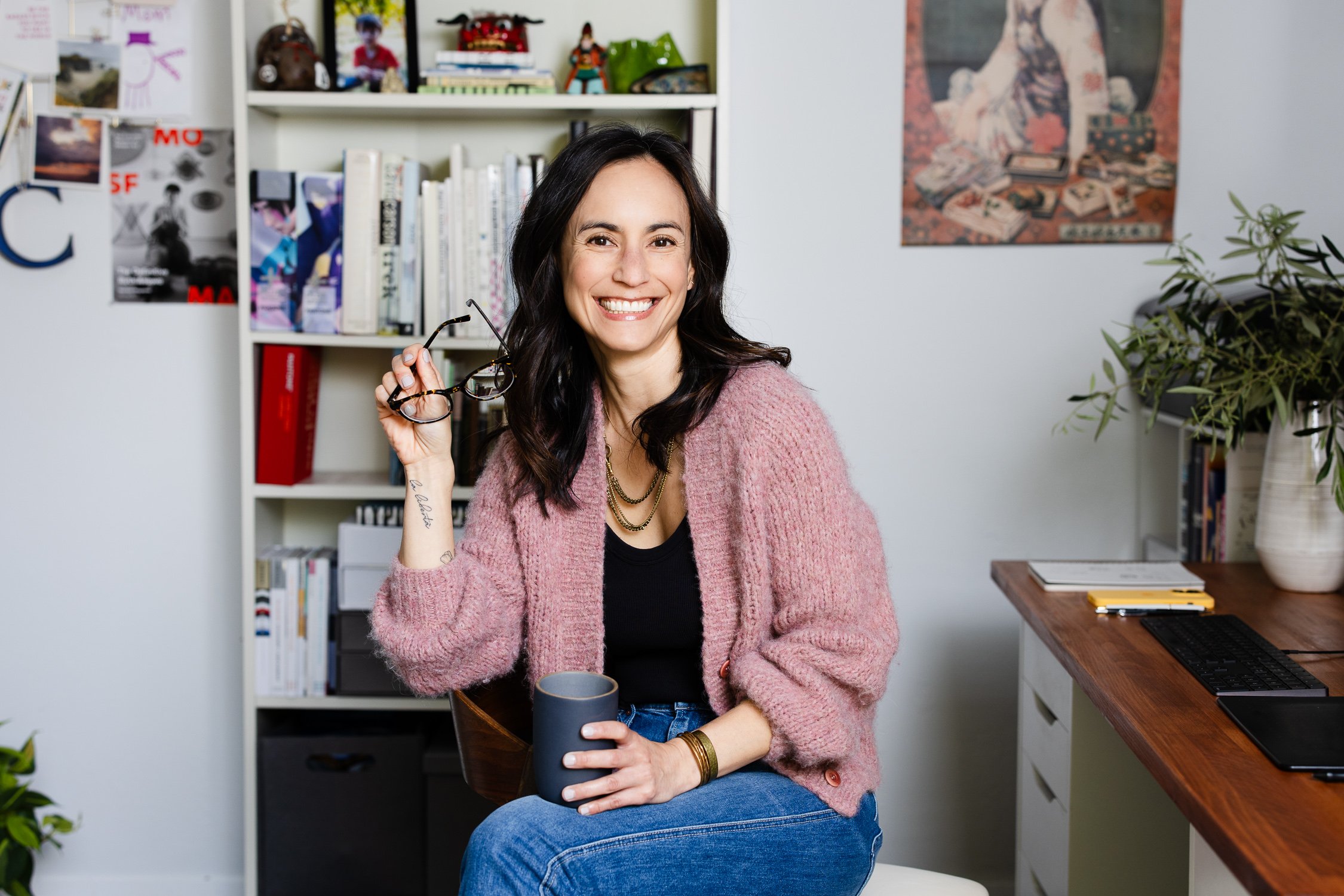 Graphic designer sitting in her backyard office holding her glasses and a cup of tea, photographed for personal brand storytelling