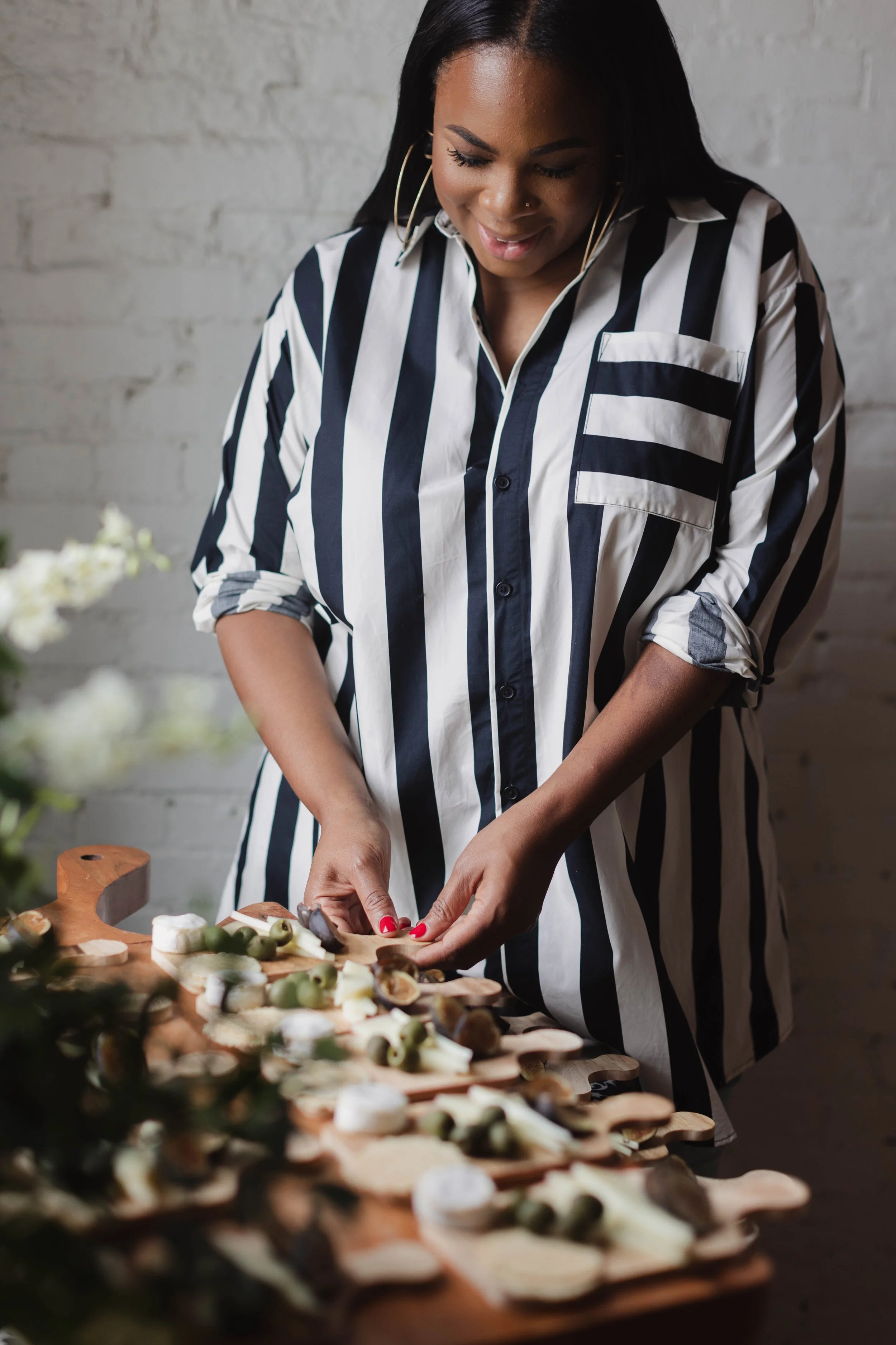 Person in striped shirt preparing a charcuterie board with cheese and olives on a wooden table.