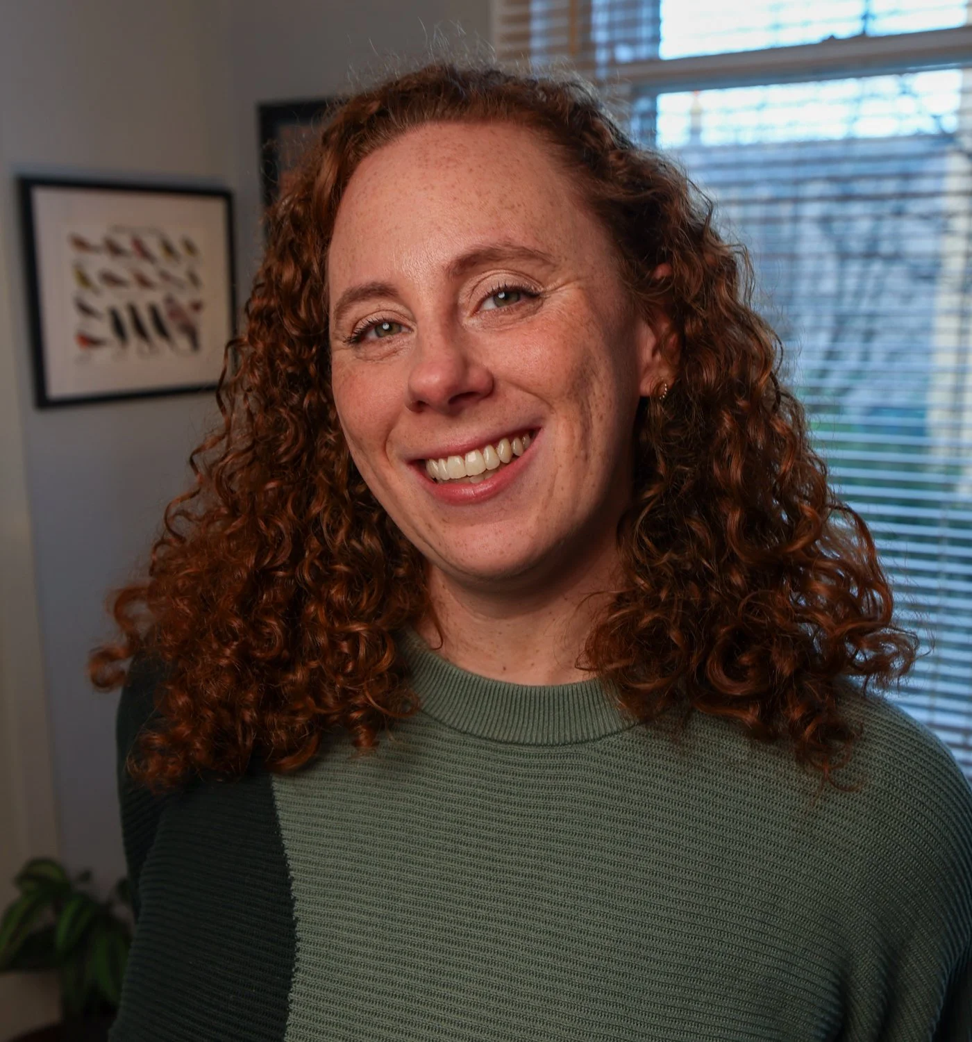 a photo of Katherine. I am white, have red curly hair, am wearing a green sweater, and am smiling