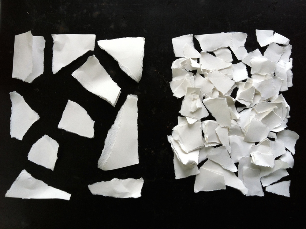 Anordnung von weissen Papierschnipseln auf schwarzem Grund