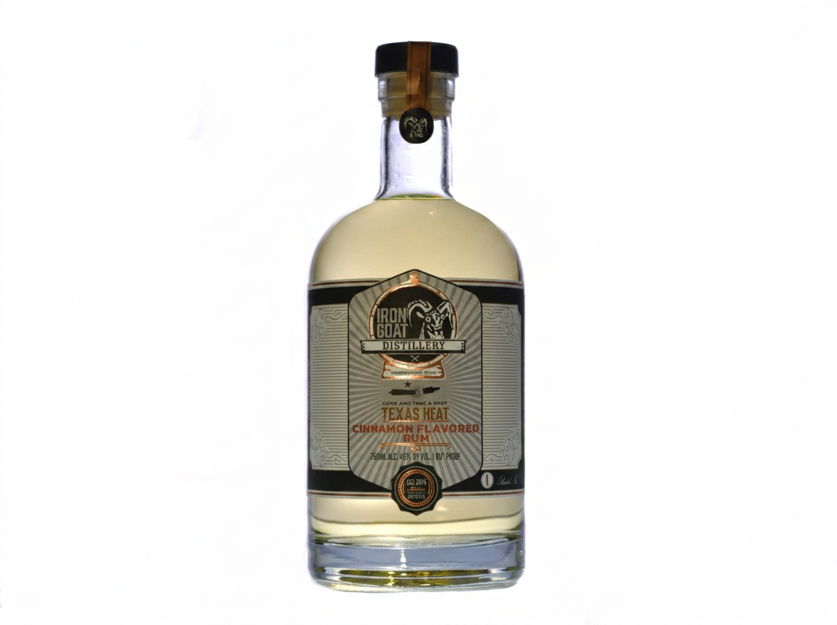 Bottle of cinnamon-flavored rum from Iron Goat Distillery, labeled 'Texas Heat,' with a black cap and a gold seal.