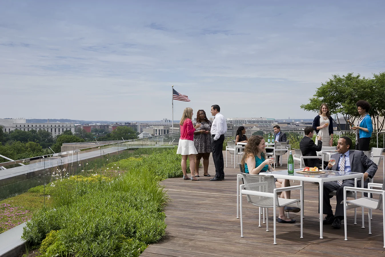 Groups seated at patio tables and standing, with skyline in background