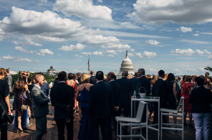 Event attendees socializing on rooftop deck, with Capitol building in background