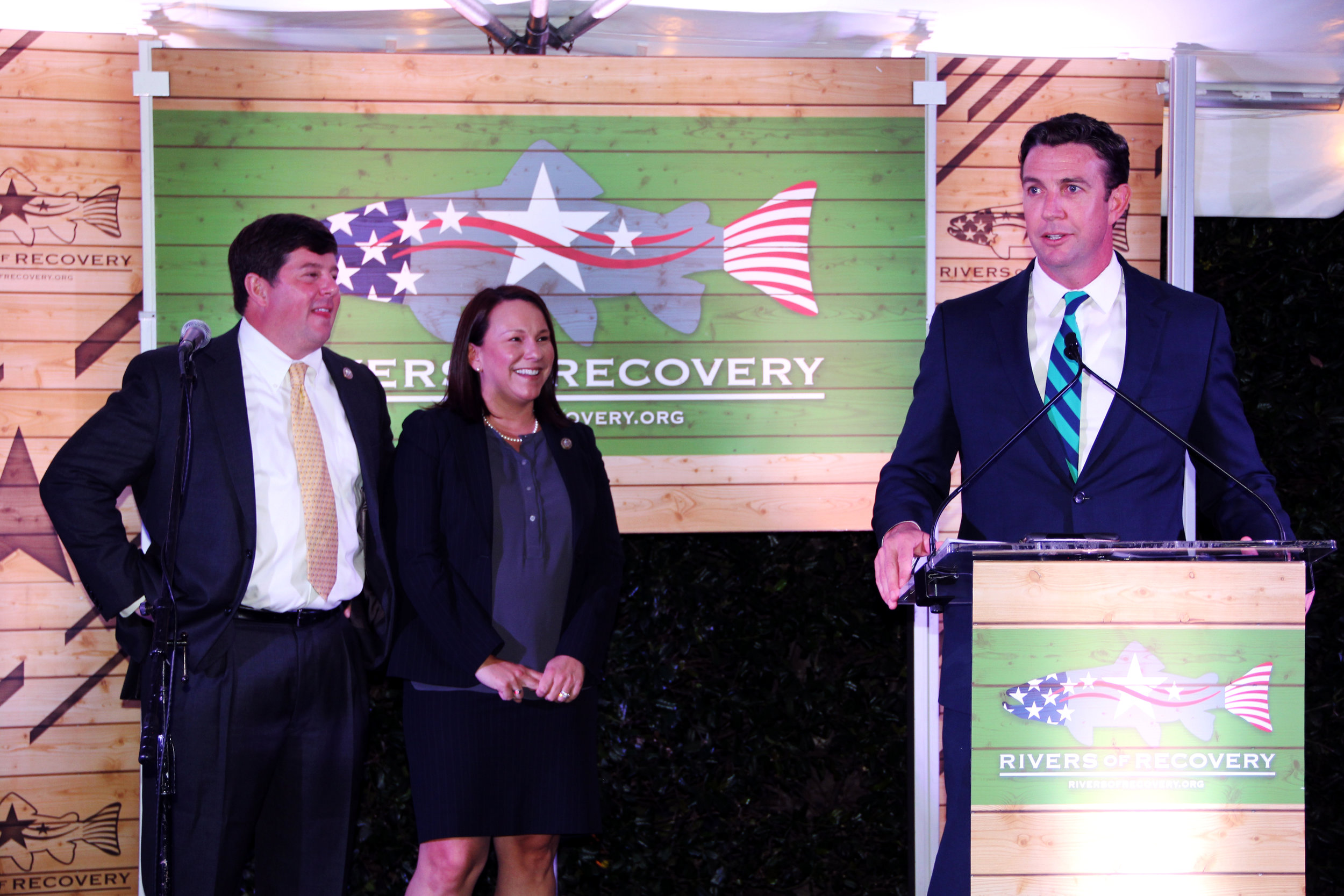 Man giving presentation at podium, with two colleagues in background