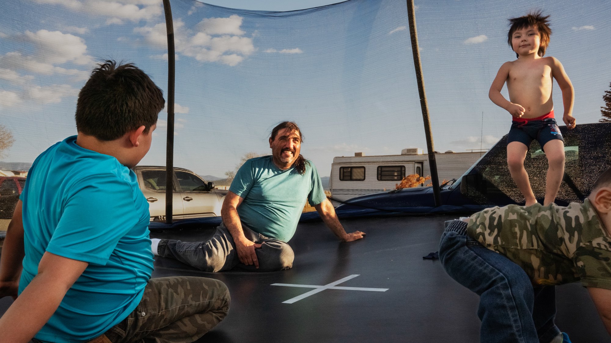   Arnold Quintana sits on a trampoline at home with his grandchildren.  