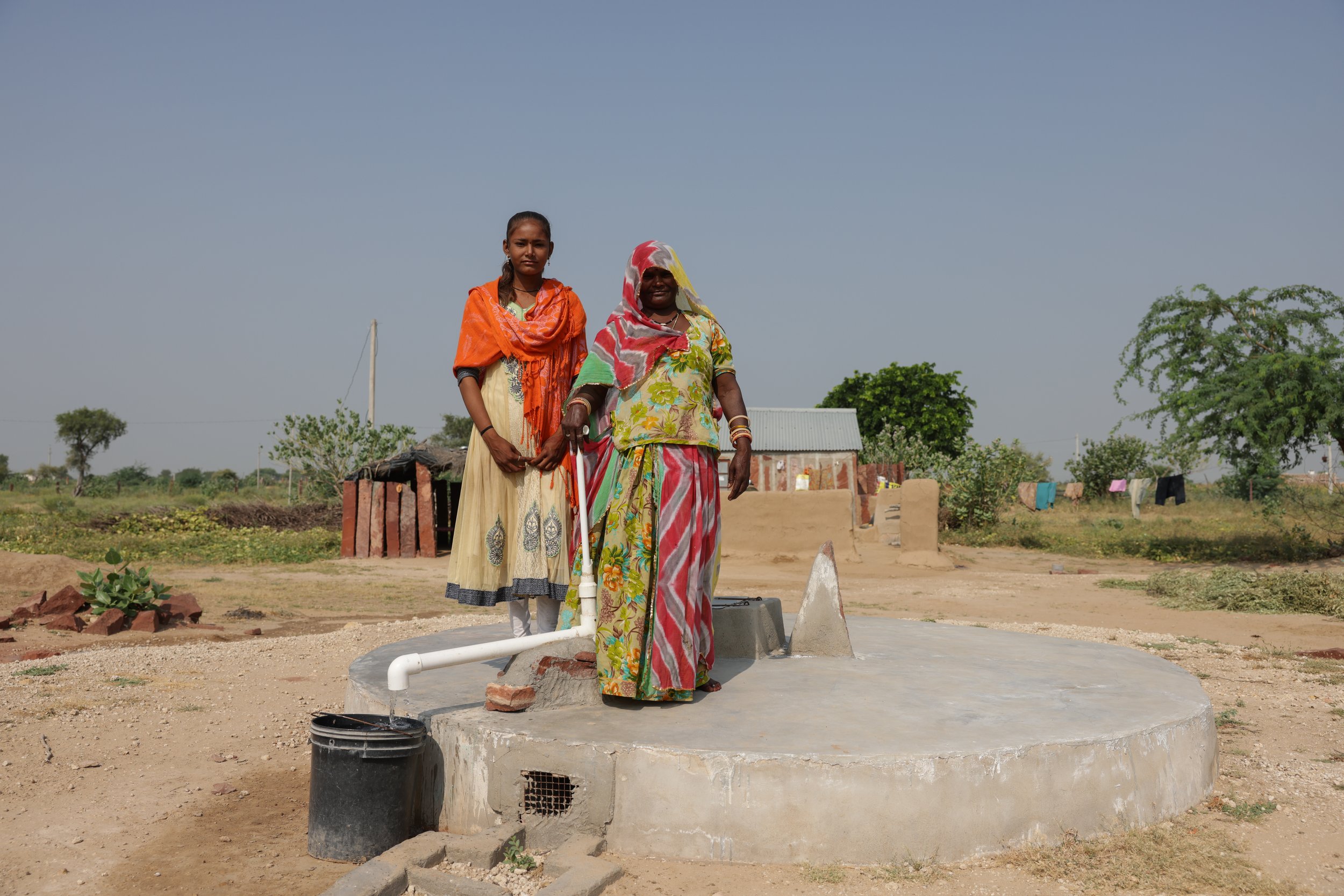 Chirmi and her daughter outside their home pumping water from a rainwater harvesting tank.