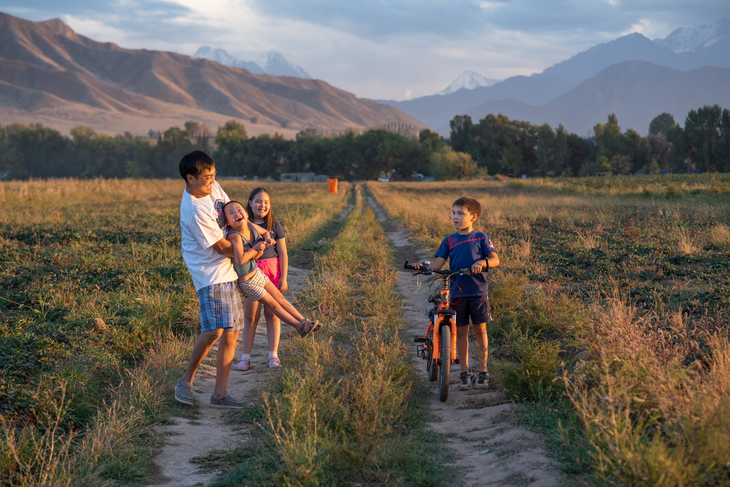 Nurmat playing with his children in the agricultural fields behind their home.