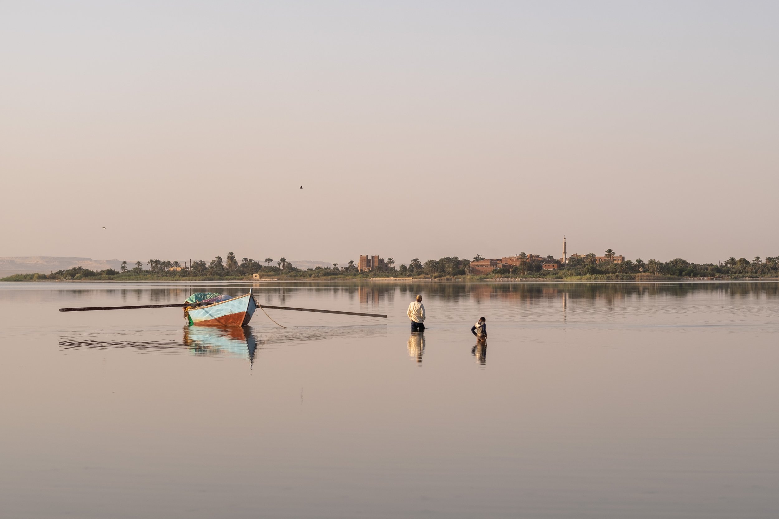 A fisherman with his son wades towards his fishing boat in Lake Qarun. September 22, 2022.