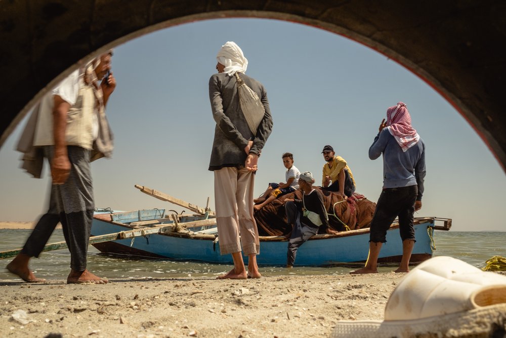 Fishermen stand on the beach before sailing out onto Lake Qarun. In the background is their vessel - a traditional boat. Fayoum, Egypt.