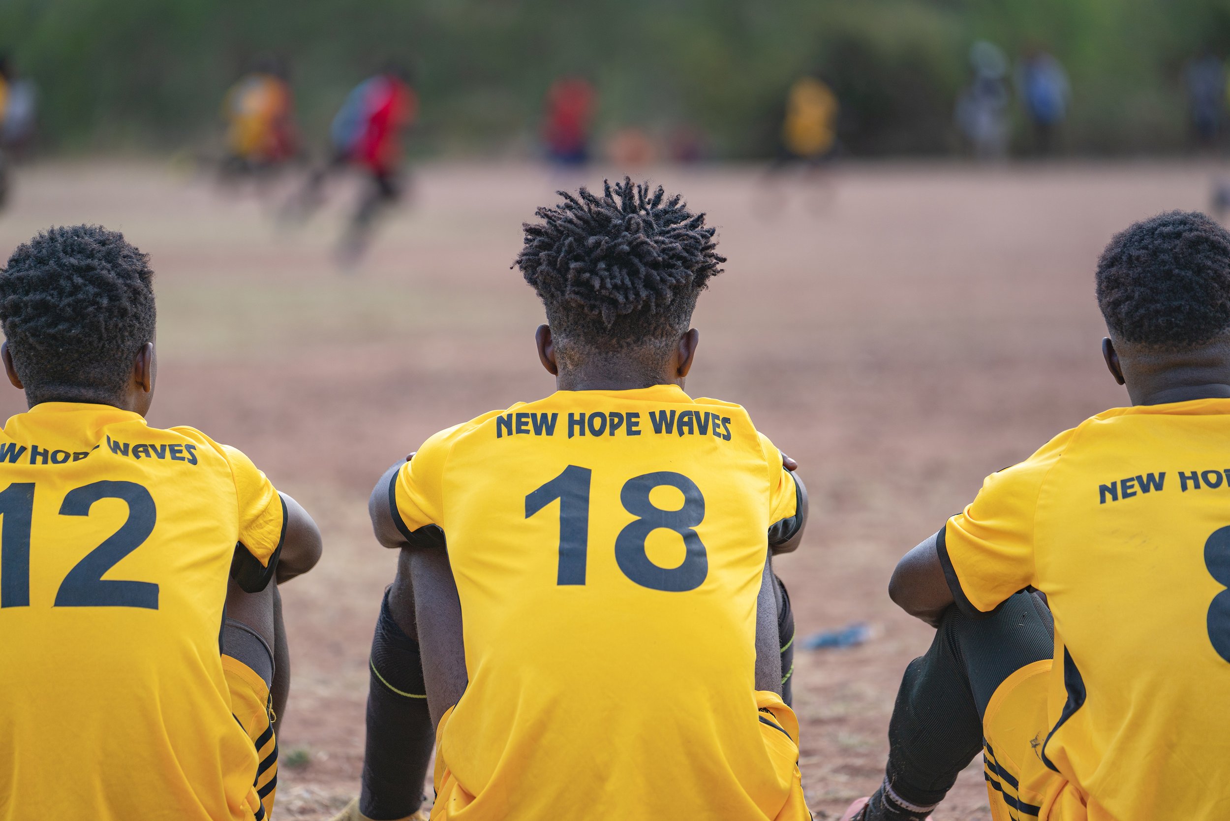  New Hope Waves Football team players waiting on the sidelines watching the community game  in Livingstone Zambia.  