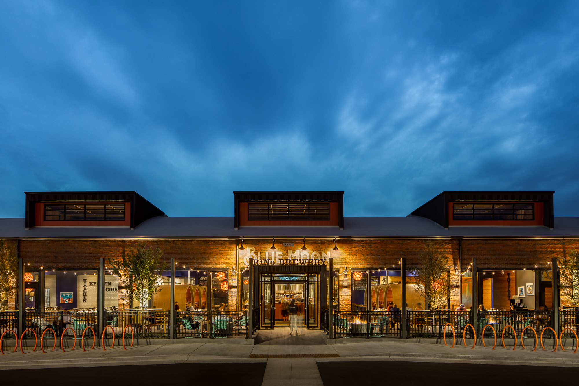 Glass garage doors connect the exterior patio to the interior, opening the building up to an informal layout made up of casual, soft seating and table settings.