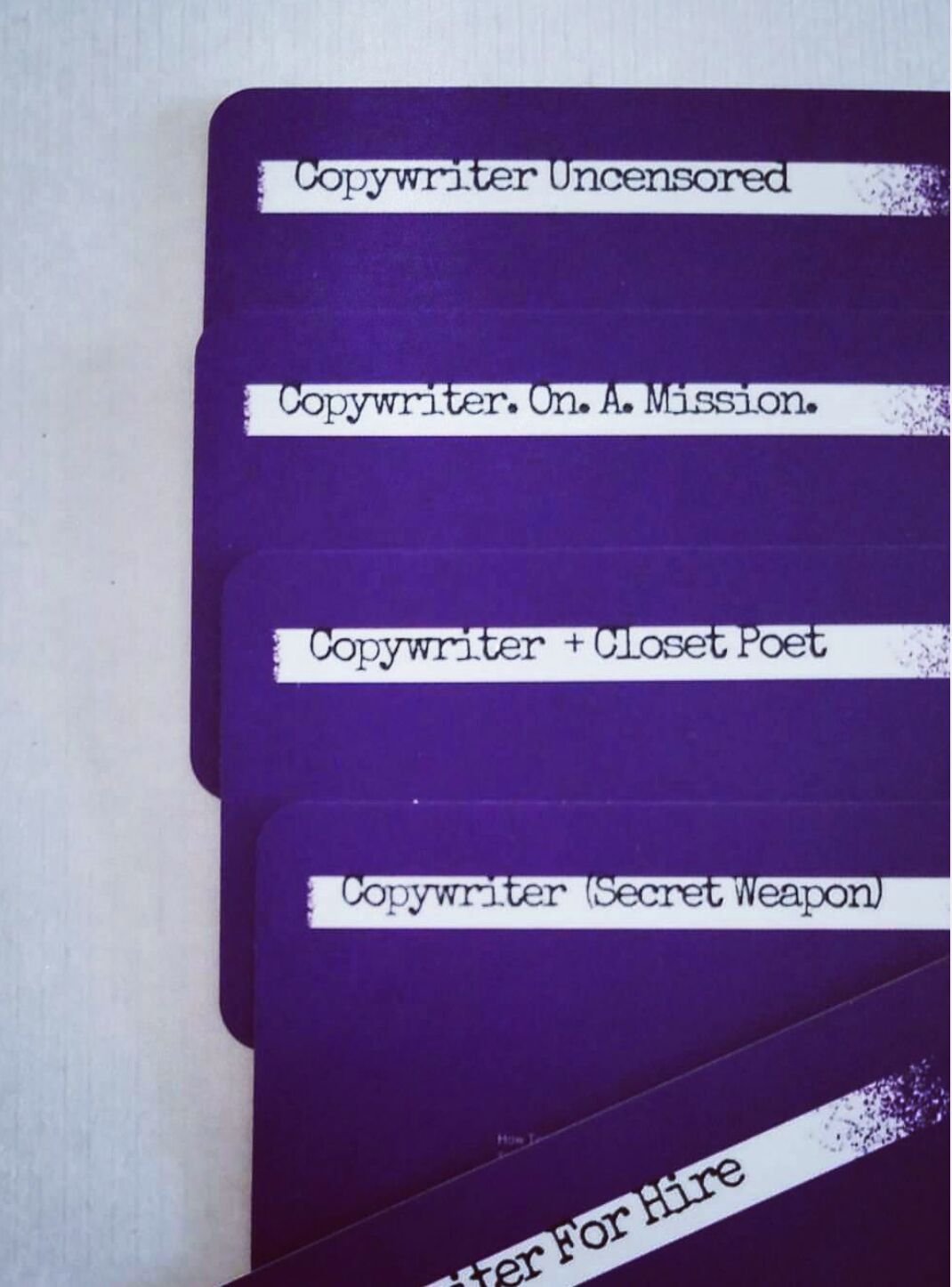 Purple business cards printed with five copywriter titles, from Copywriter Uncensored to Copywriter For Hire